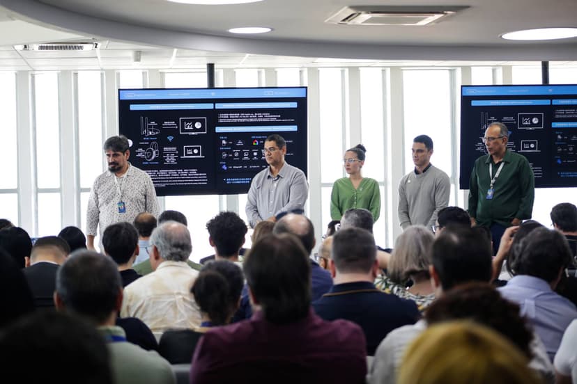 Equipe apresentando projeto no palco com tela exibindo informações técnicas no evento